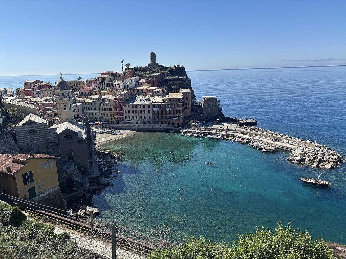 Přírodní přístav ve Vernazze v Cinque Terre — tyrkysová voda, barevné domy a věž hradu Doria nad vesnicí